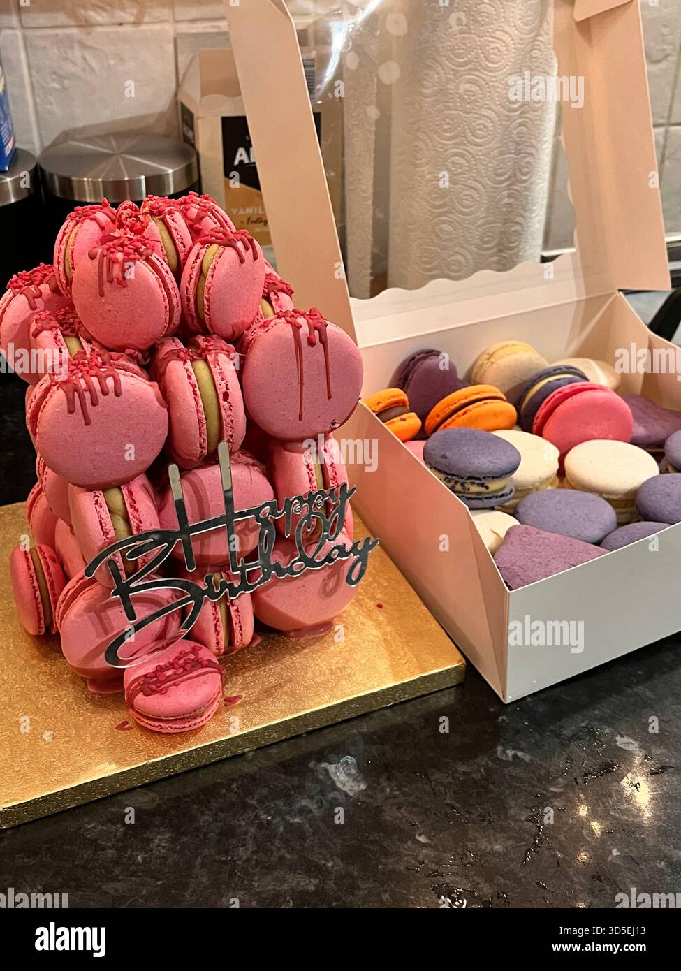 A decorative arrangement of pink macarons in a box, displayed with a birthday topper and additional pastries. - Smartphone Captured Stock Image