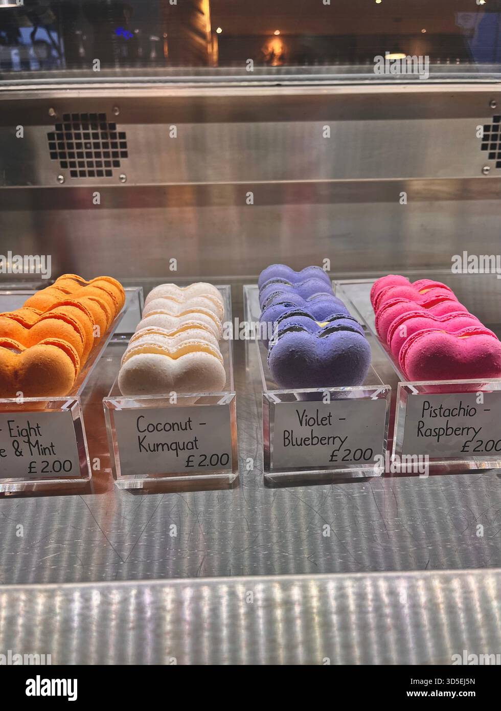 A glass bakery display filled with colorful macarons labeled with different flavors. The vibrant dessert showcase is photographed in Hull, England. - Smartphone Captured Stock Image