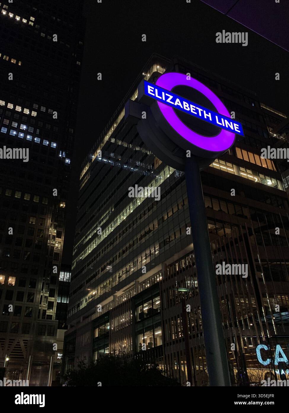 Close-up of the illuminated Elizabeth Line roundel set against modern glass skyscrapers at night in London, England. - Smartphone Captured Stock Image