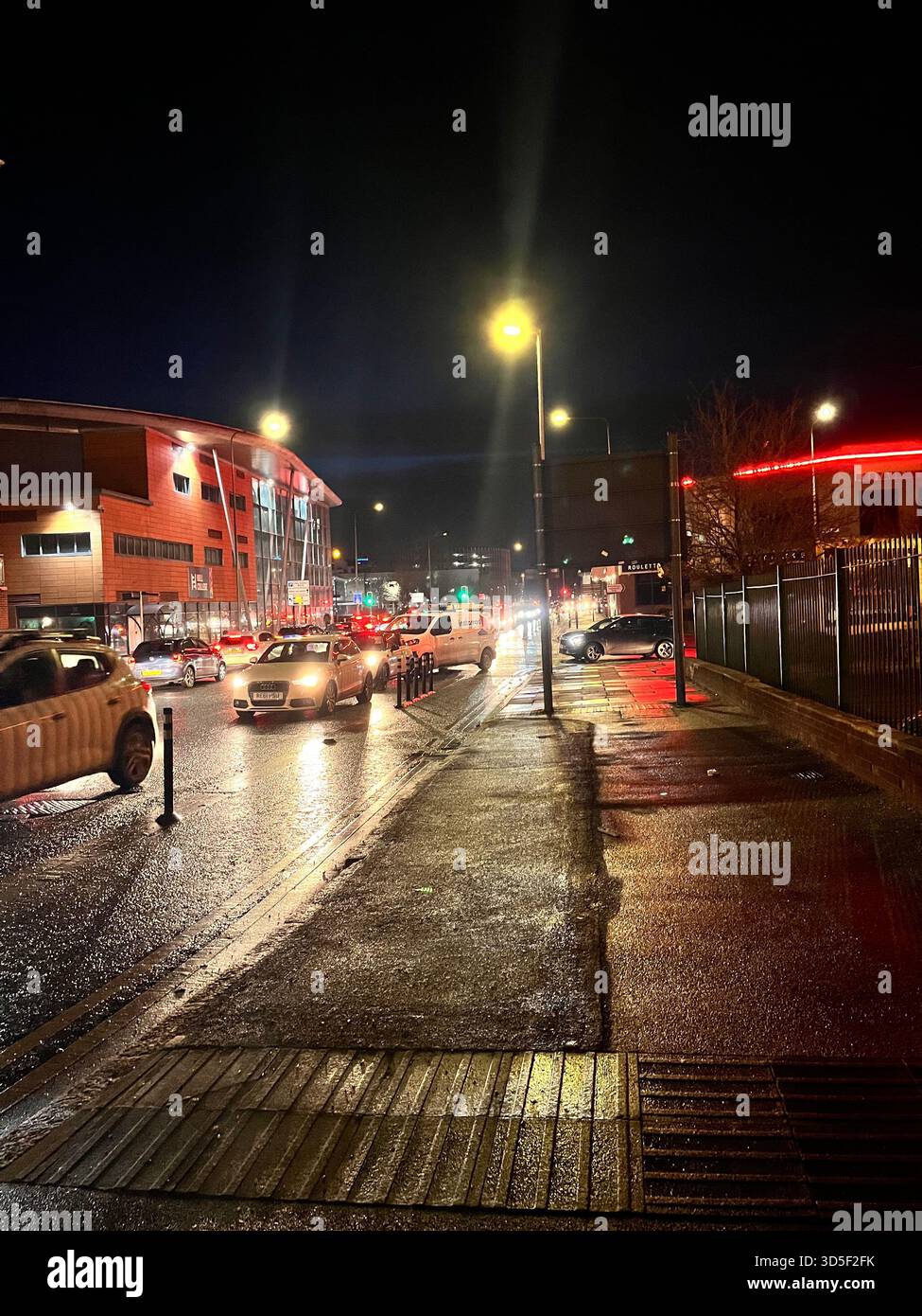 Wet urban street in Hull, England at night with car traffic, streetlights, and glowing reflections on the pavement. - Smartphone Captured Stock Image