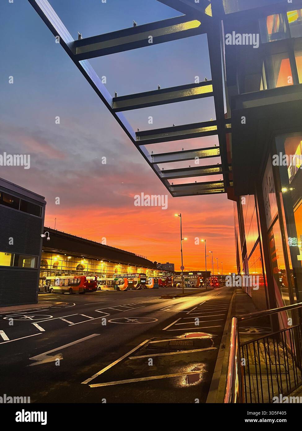 Modern bus station in Hull, England, photographed at sunset with dramatic orange sky reflections on wet pavement. - Smartphone Captured Stock Image