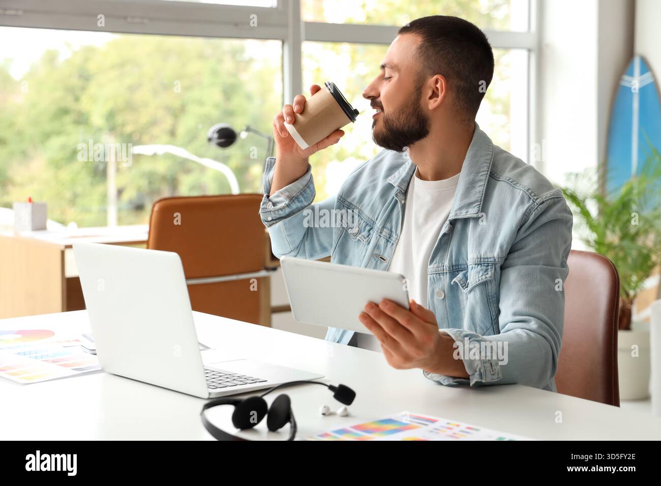 Young man drinking coffee and using tablet for online work at home Stock Photo