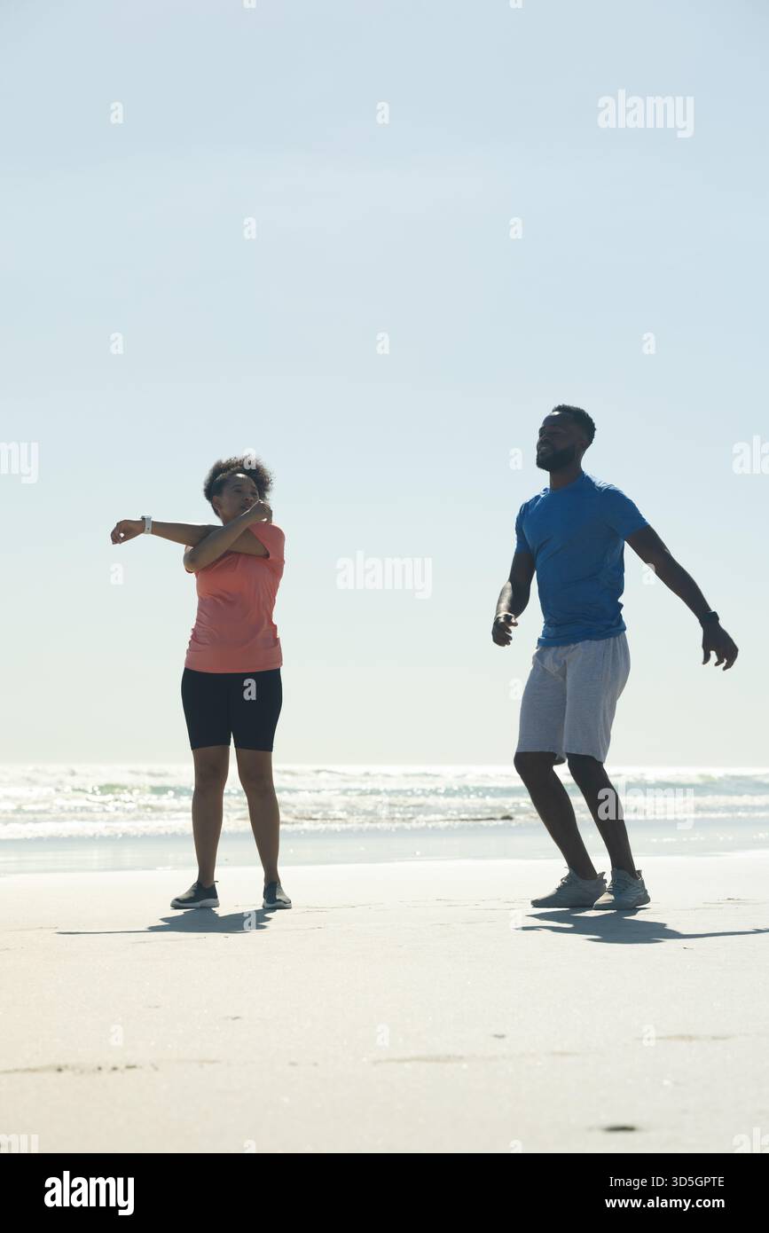 African American couple exercising on beach, stretching and jogging together Stock Photo