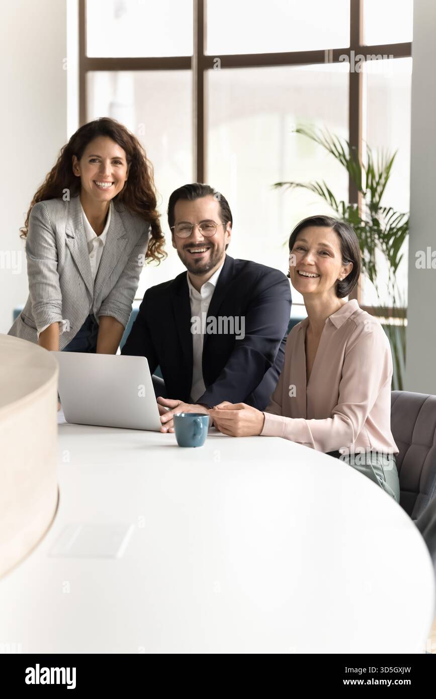 Three smiling diverse business colleagues using notebook looking at camera Stock Photo