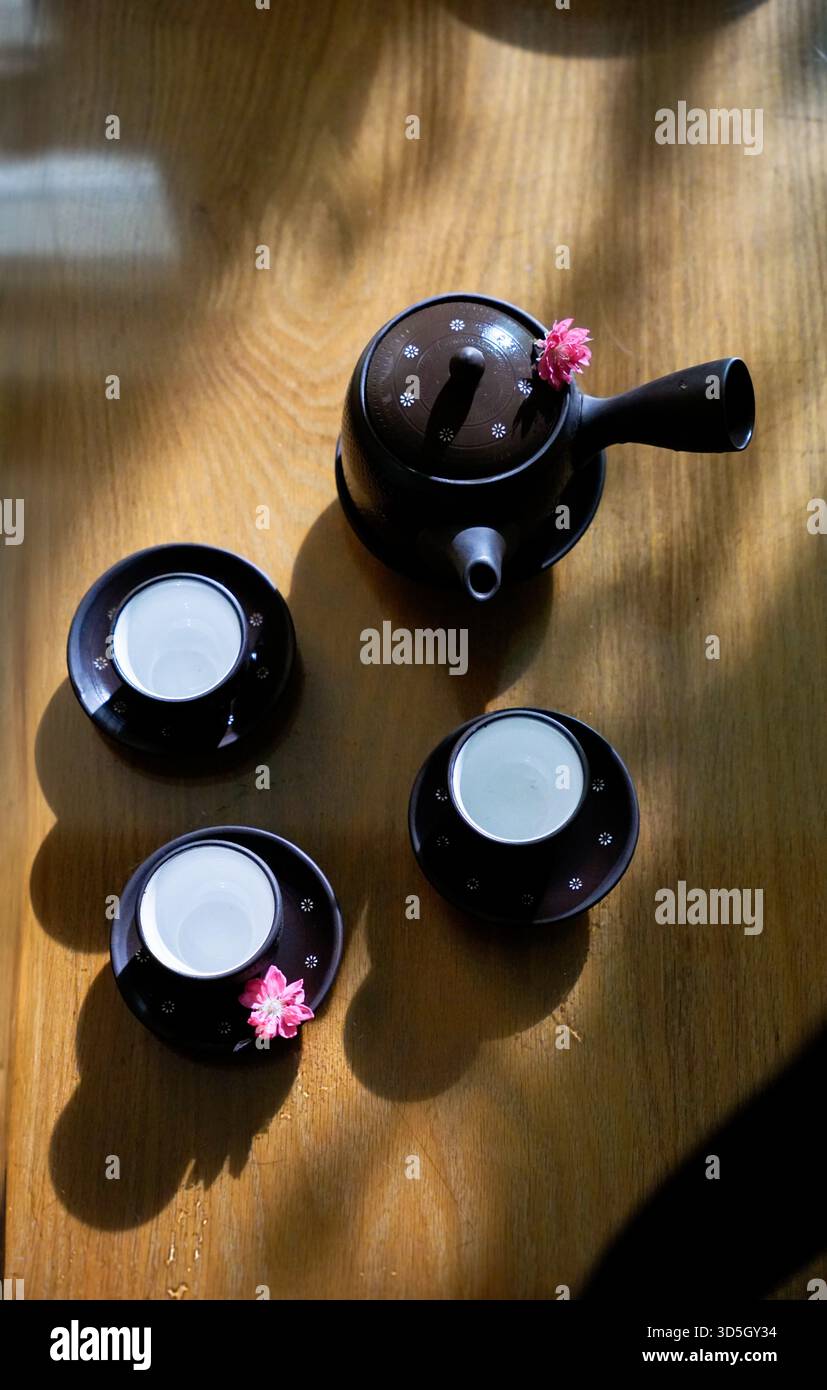 Flat lay photo of ceramic tea pot and three tea cups on wood table under sunlight Stock Photo