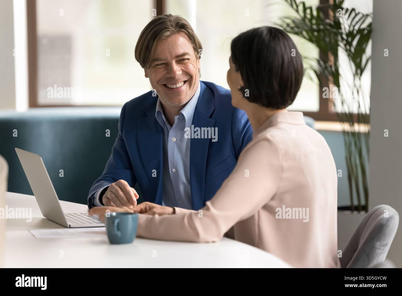 Two happy professionals collaborate on project using laptop at workplace Stock Photo