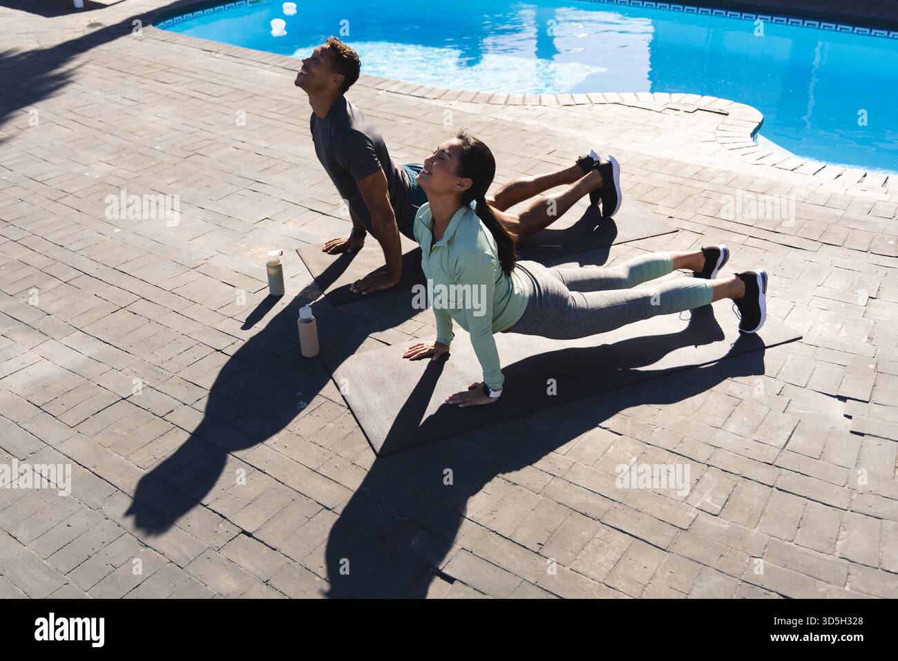 Couple practicing yoga by pool, stretching on mats under morning sun Stock Photo