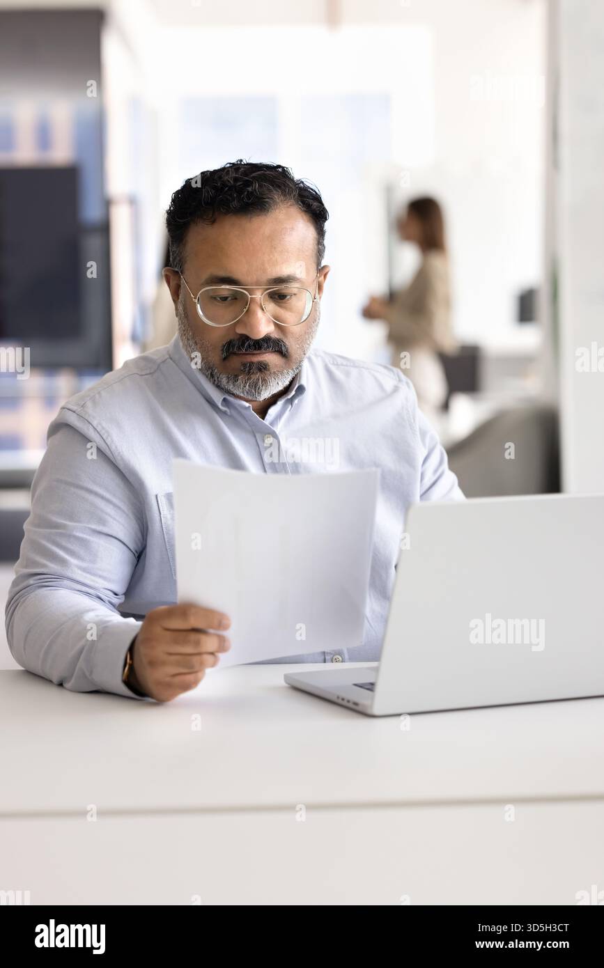 Focused busy senior Indian businessman analyzing financial document Stock Photo