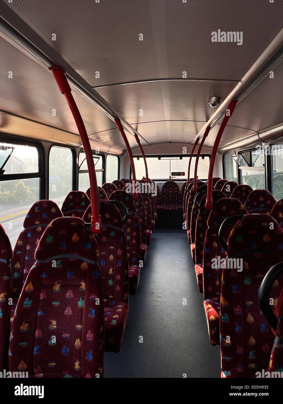 Interior of a public city bus with red patterned seats and handrails, photographed in Hull, England. Empty passenger transport scene - Smartphone Captured Stock Image