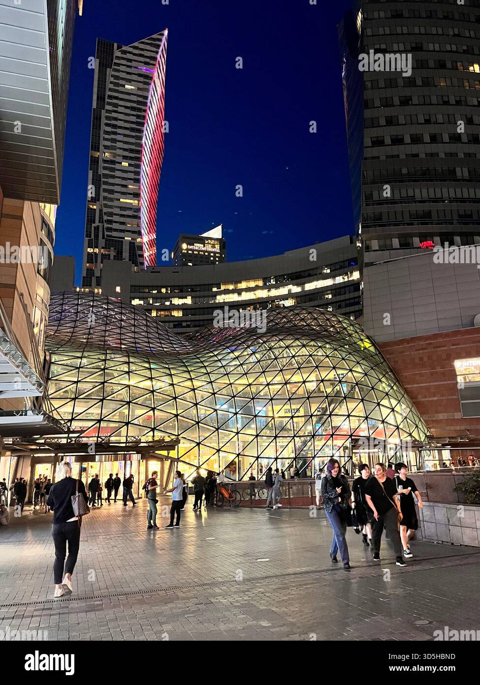 Night view of Złote Tarasy shopping mall with illuminated glass roof and people walking nearby in Warsaw, Poland. - Smartphone Captured Stock Image