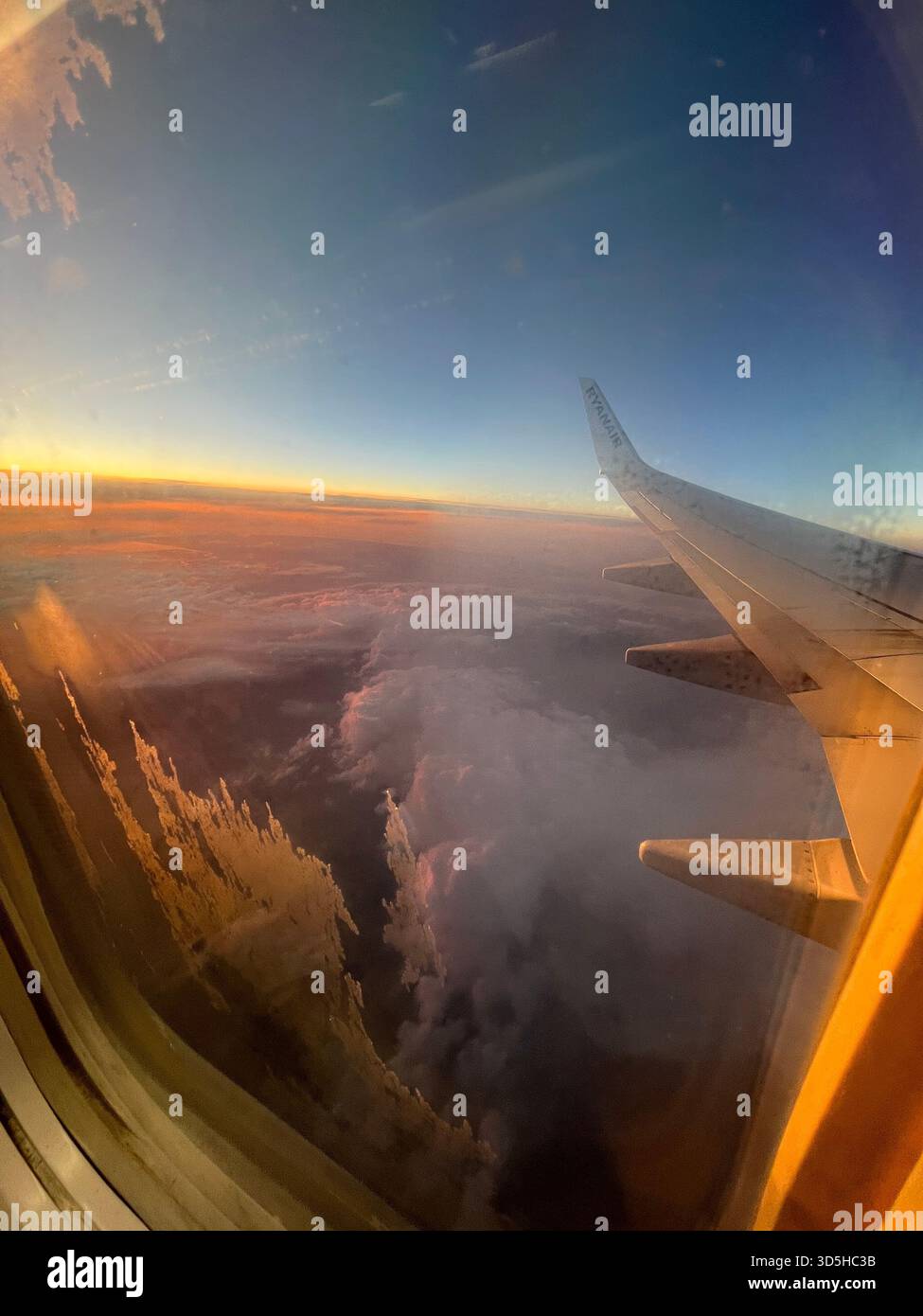Aerial view from an airplane window showing clouds and warm sunset light. Atmospheric travel image symbolizing journey, freedom, aviation, - Smartphone Captured Stock Image
