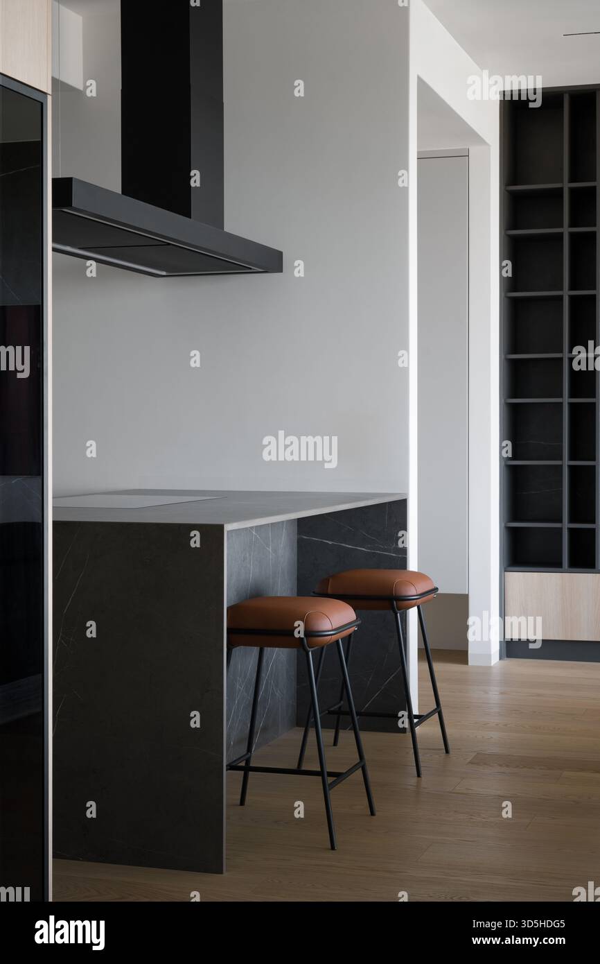 Interior of a modern and stylish kitchen featuring a dark marble island with a breakfast bar. Two elegant bar stools with brown leather seats and blac Stock Photo