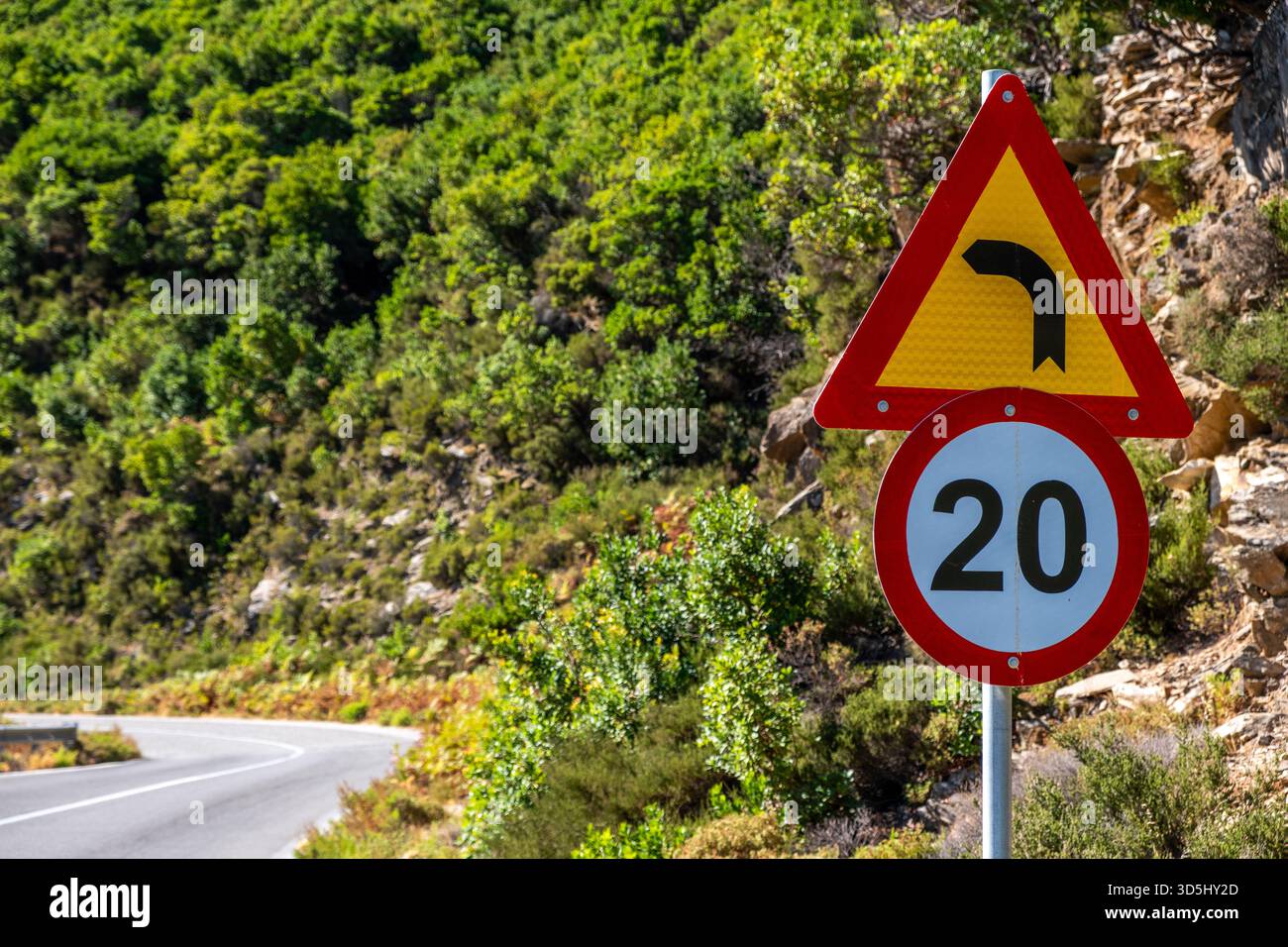 Sharp curve warning with 20 speed limit sign beside sunny winding road ...