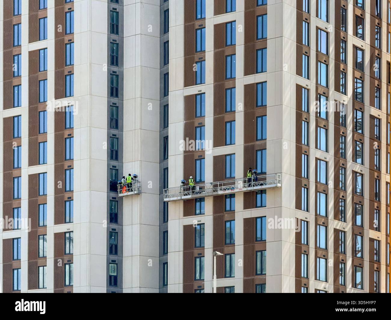 Cardiff, Wales, UK - 15 August 2025: Construction workers working on platforms on the side of a new block of apartments in Cardiff city centre - Smartphone Captured Stock Image