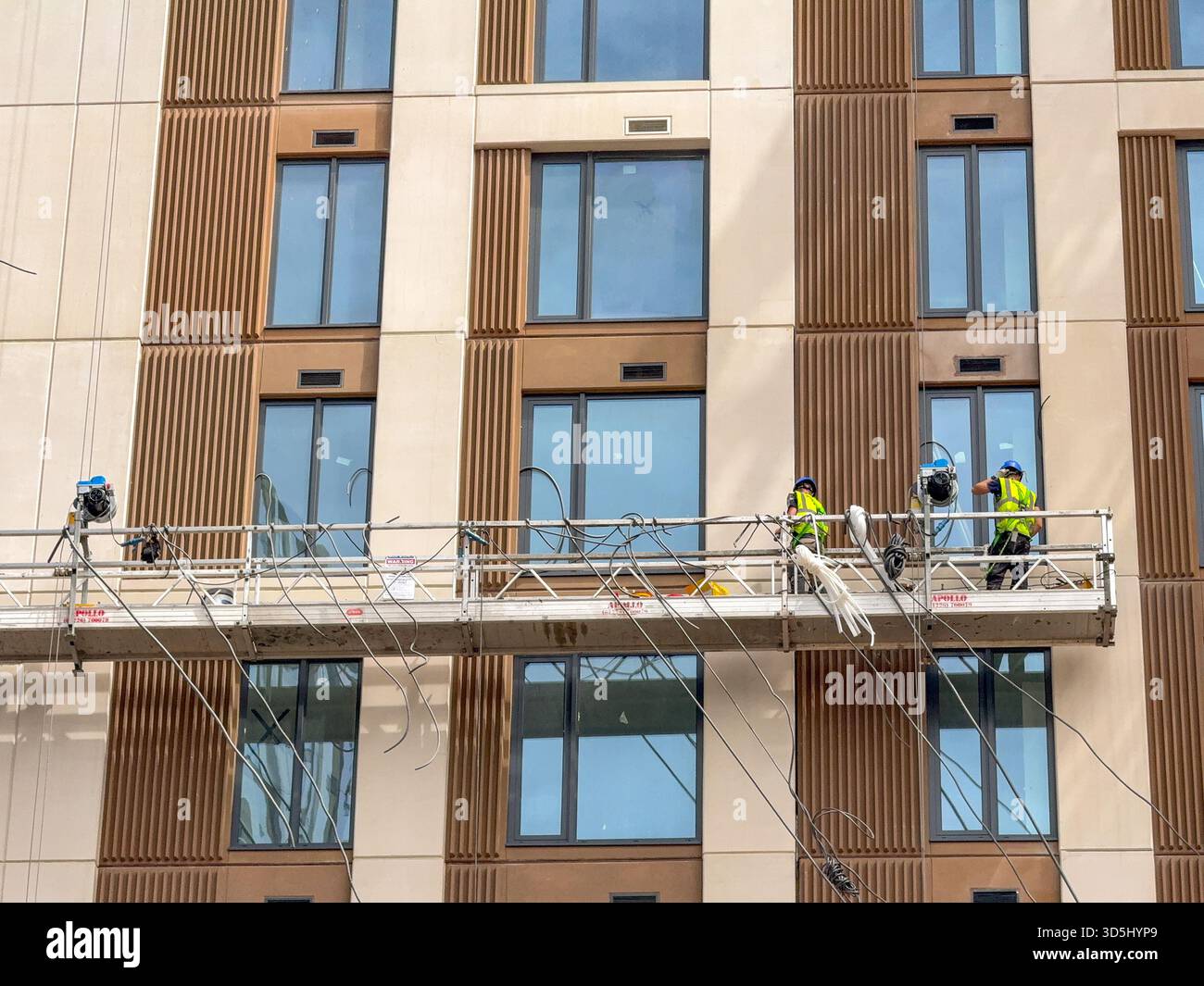 Cardiff, Wales, UK - 16 July 2025: Construction workers on a platform suspended high up on the outside of a new block of flats in Cardiff city centre. - Smartphone Captured Stock Image
