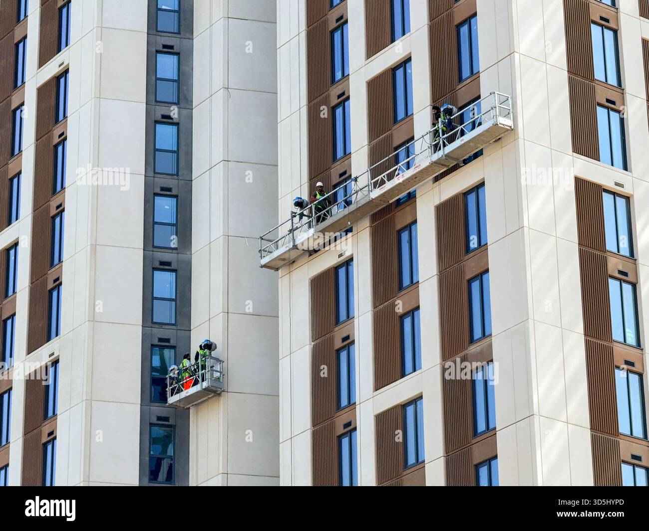 Cardiff, Wales, UK - 15 August 2025: Construction workers working on platforms on the side of a new block of apartments in Cardiff city centre - Smartphone Captured Stock Image
