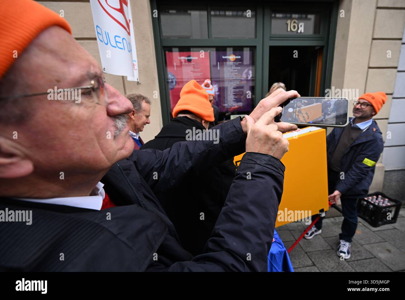 Munich, Germany. 16th Nov, 2025. Former Munich mayor Christian Ude (SPD, l) uses his cell phone to record the loading of the Lach- und Schießgesellschaft sign onto a trolley in front of the Lach- und Schießgesellschaft premises in Haimhauserstrasse. The Munich Lach- und Schießgesellschaft moves from Haimhauserstrasse to the Fat Cat (Alter Gasteig) on Rosenheimer Platz by subway and suburban train. Credit: Felix Hörhager/dpa/Alamy Live News Stock Photo