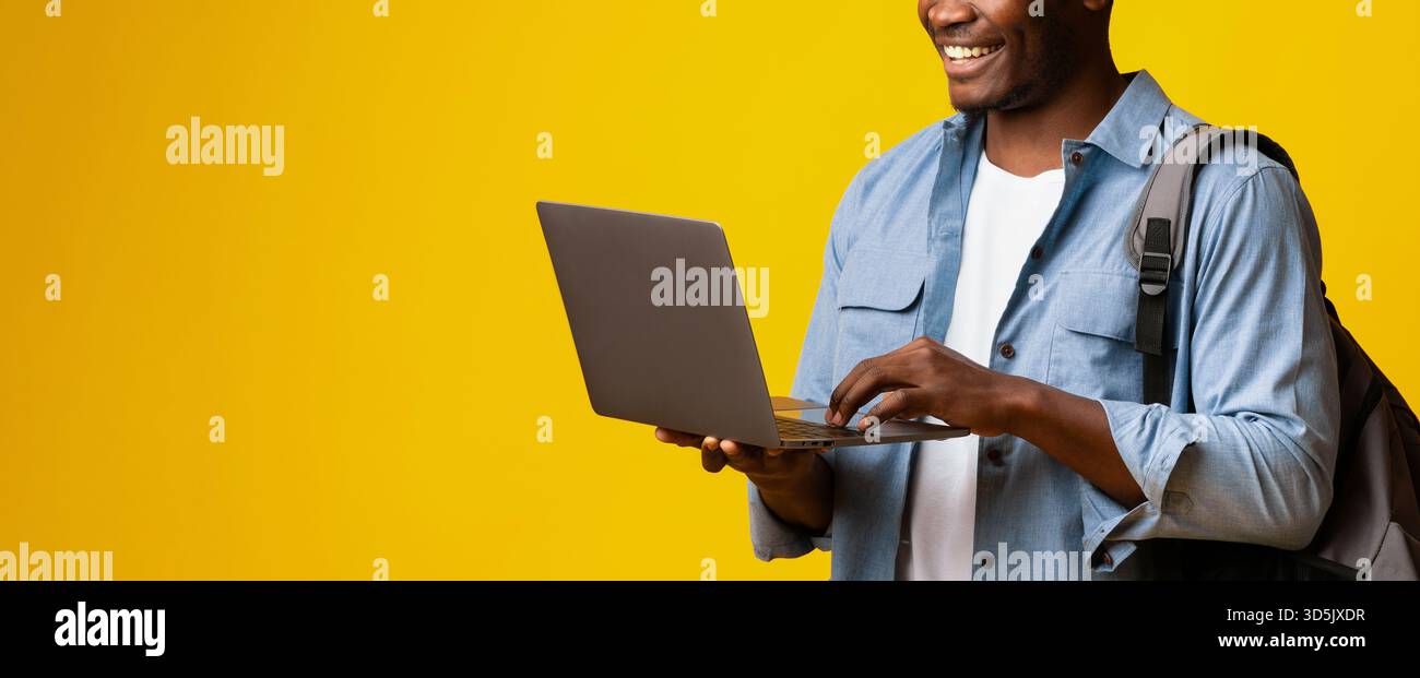 Young Man Smiling While Using Laptop Against Bright Yellow Background in Modern Setting Stock Photo