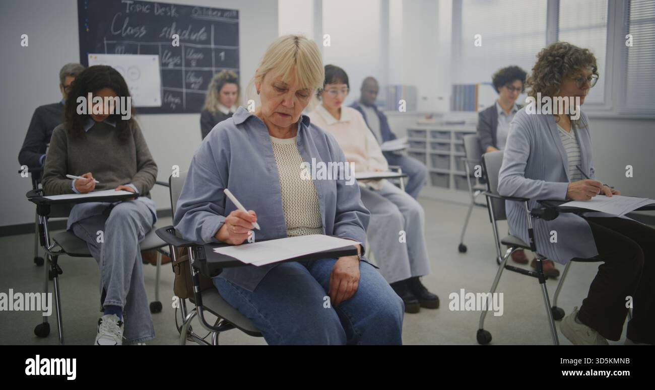 Multicultural Group Of Mature Students Taking Notes During Lesson in Bright Classroom. Students Note Lectures Given by Teacher. Concept Continuing Education, Adult Learning, and Knowledge Development. Stock Photo