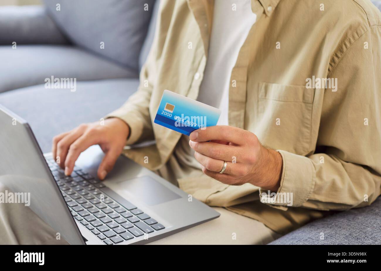 Man with laptop and credit card at home, verifying online payment details Stock Photo