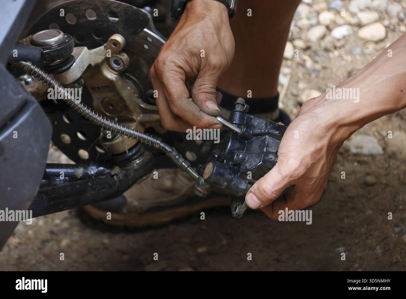 Focused man with dirty hands doing repair on vehicle suspension. mechanic using tool for maintenance on an off road machine, showing concentrated hand Stock Photo