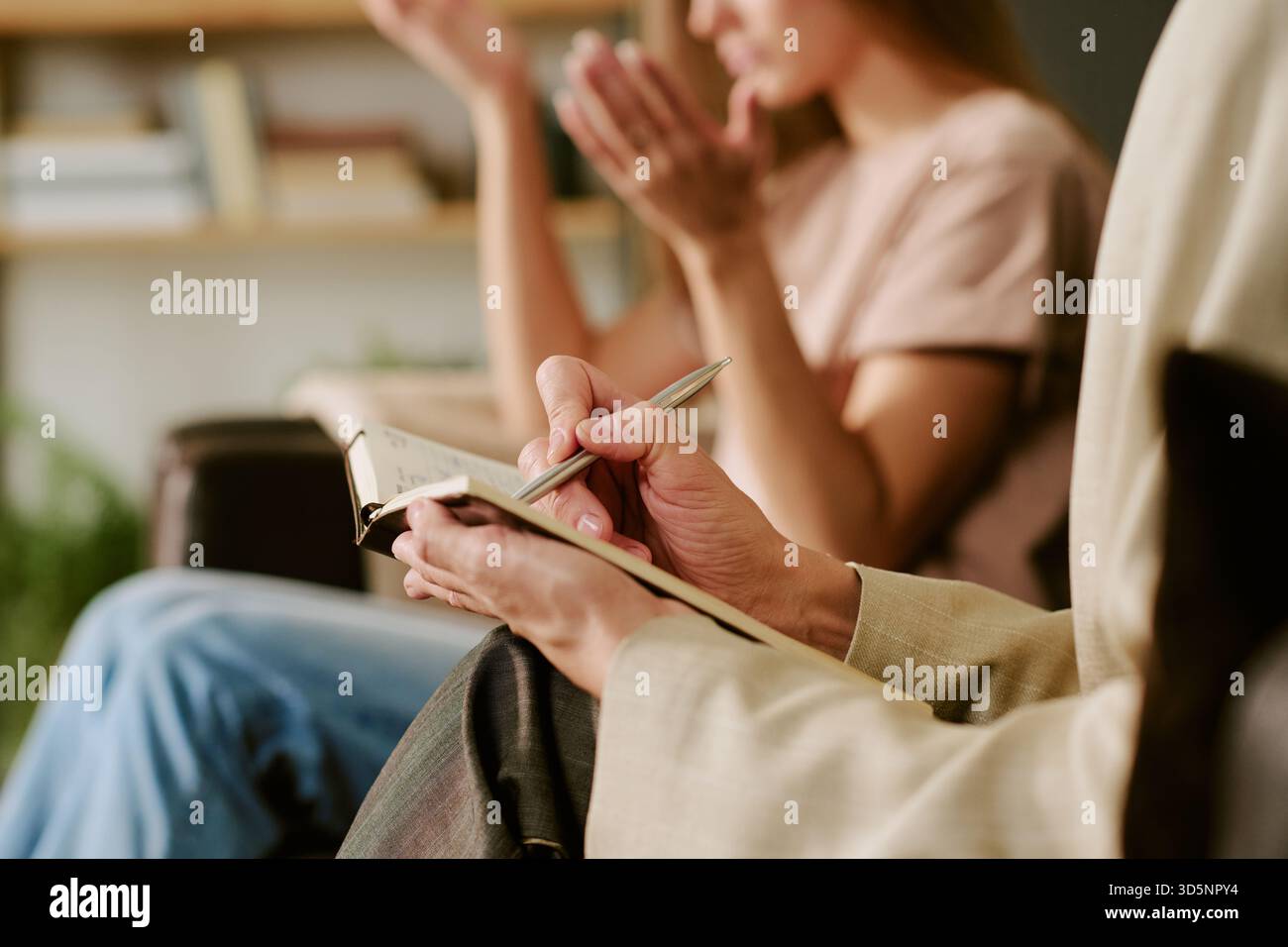 Caucasian Young Woman Gesturing While Psychologist Taking Notes during Session Stock Photo