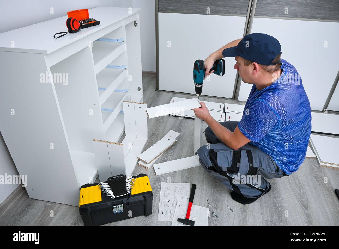 Man using power tool for home improvement, assembling white cabinet in ...