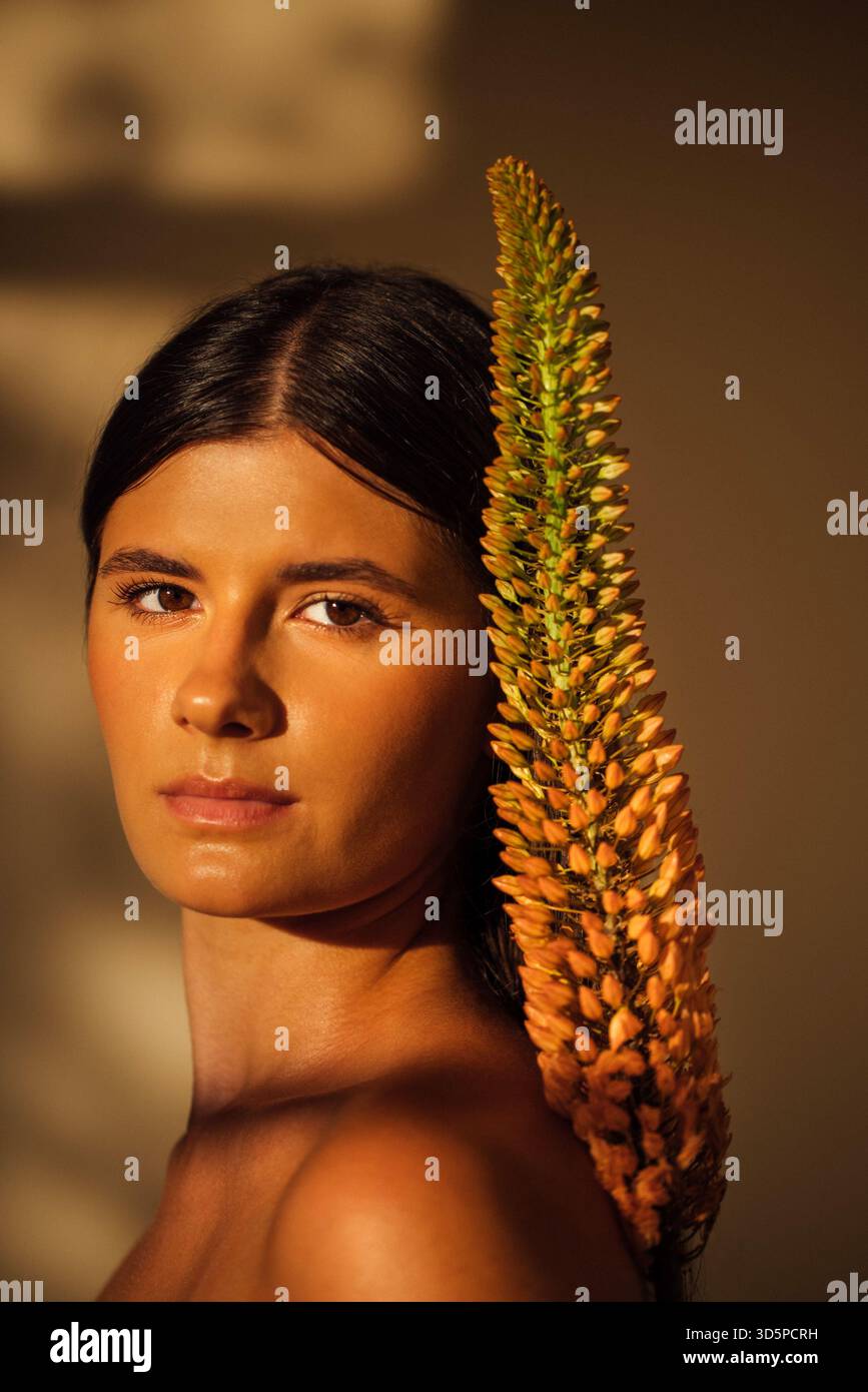 Dark-haired female model poses elegantly with a unique plant accent, highlighting her features and the interplay of light and shadow in a serene atmos Stock Photo