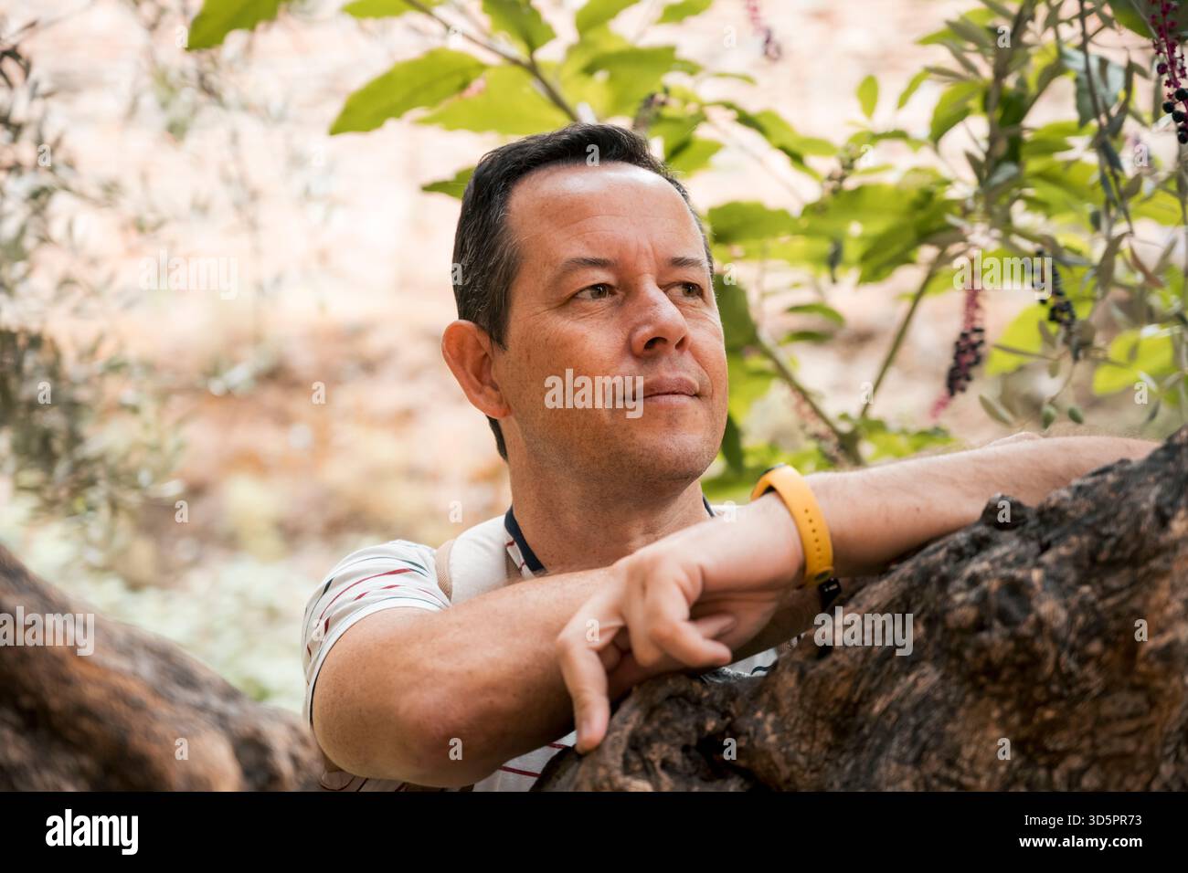Thoughtful man leaning on tree in outdoor natural setting Stock Photo