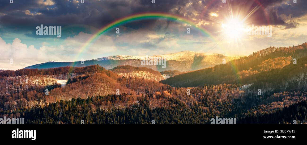 panorama of distant mountain ridge with snowy top at sunset. beautiful forested rolling hill of a countryside in front in evening light. timeless nost Stock Photo