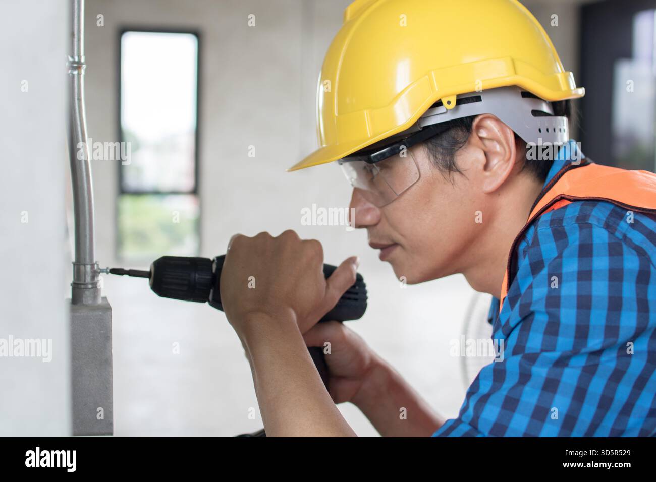 A construction worker is using a large,  hammer drill screwing  a screw into the wall using a cordless screwdriver Stock Photo