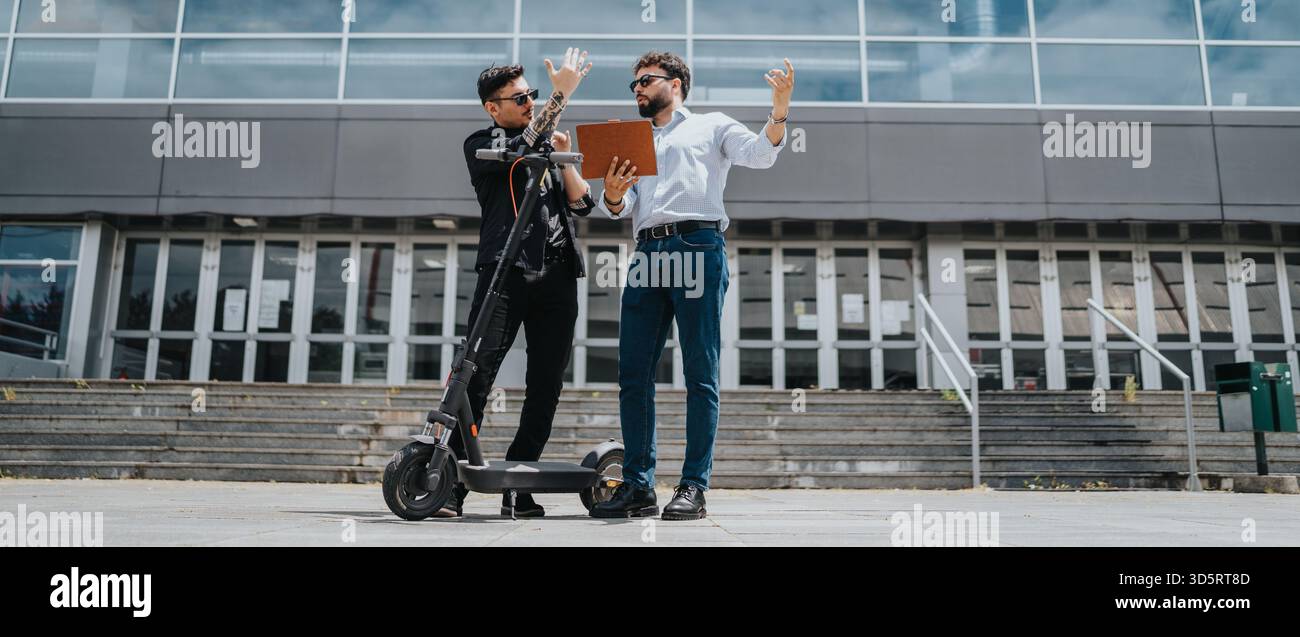 Two colleagues discussing work details while using an electric scooter outdoors. Stock Photo