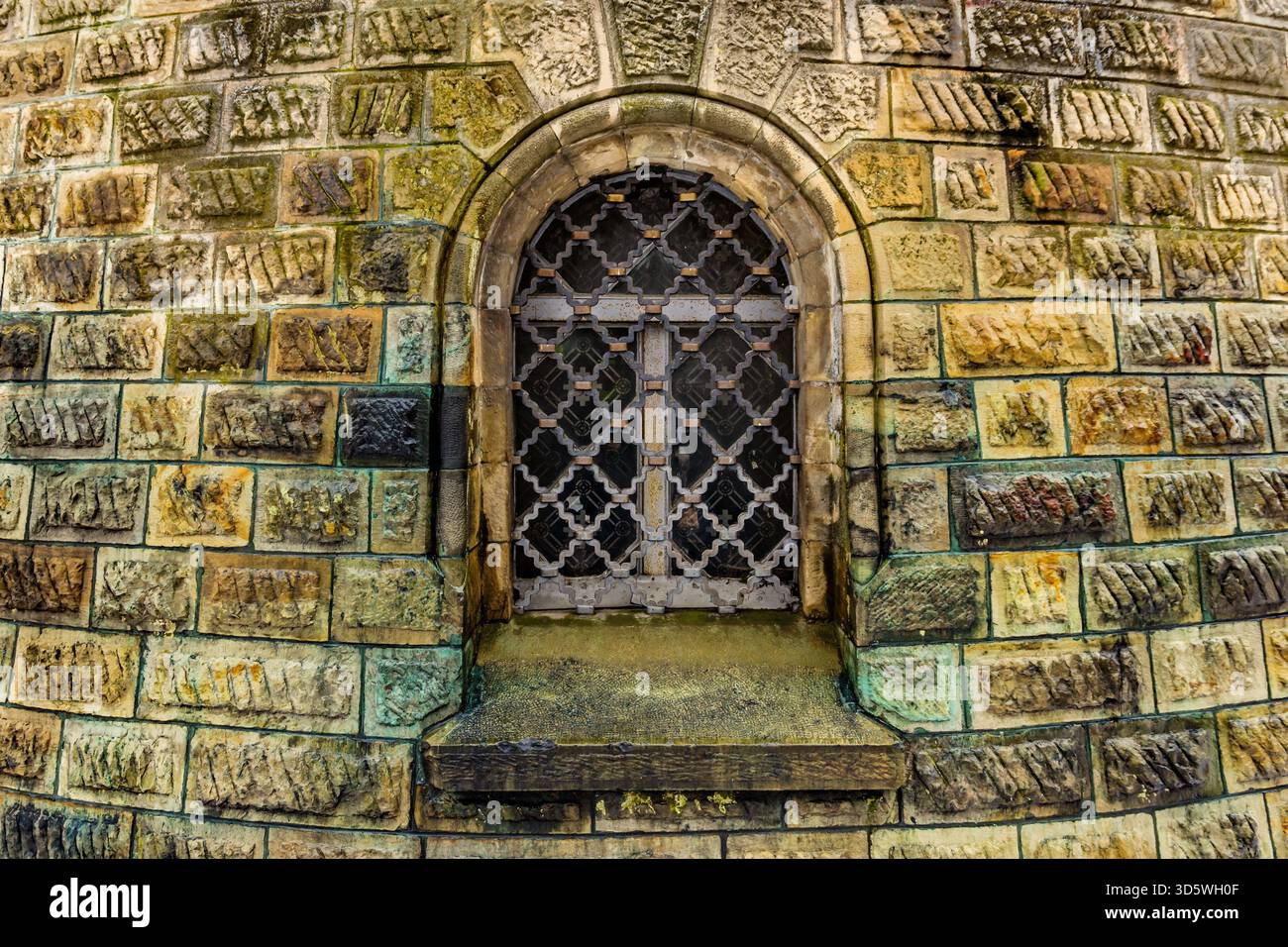 A small arched window with wrought iron grille sits in a weathered ...