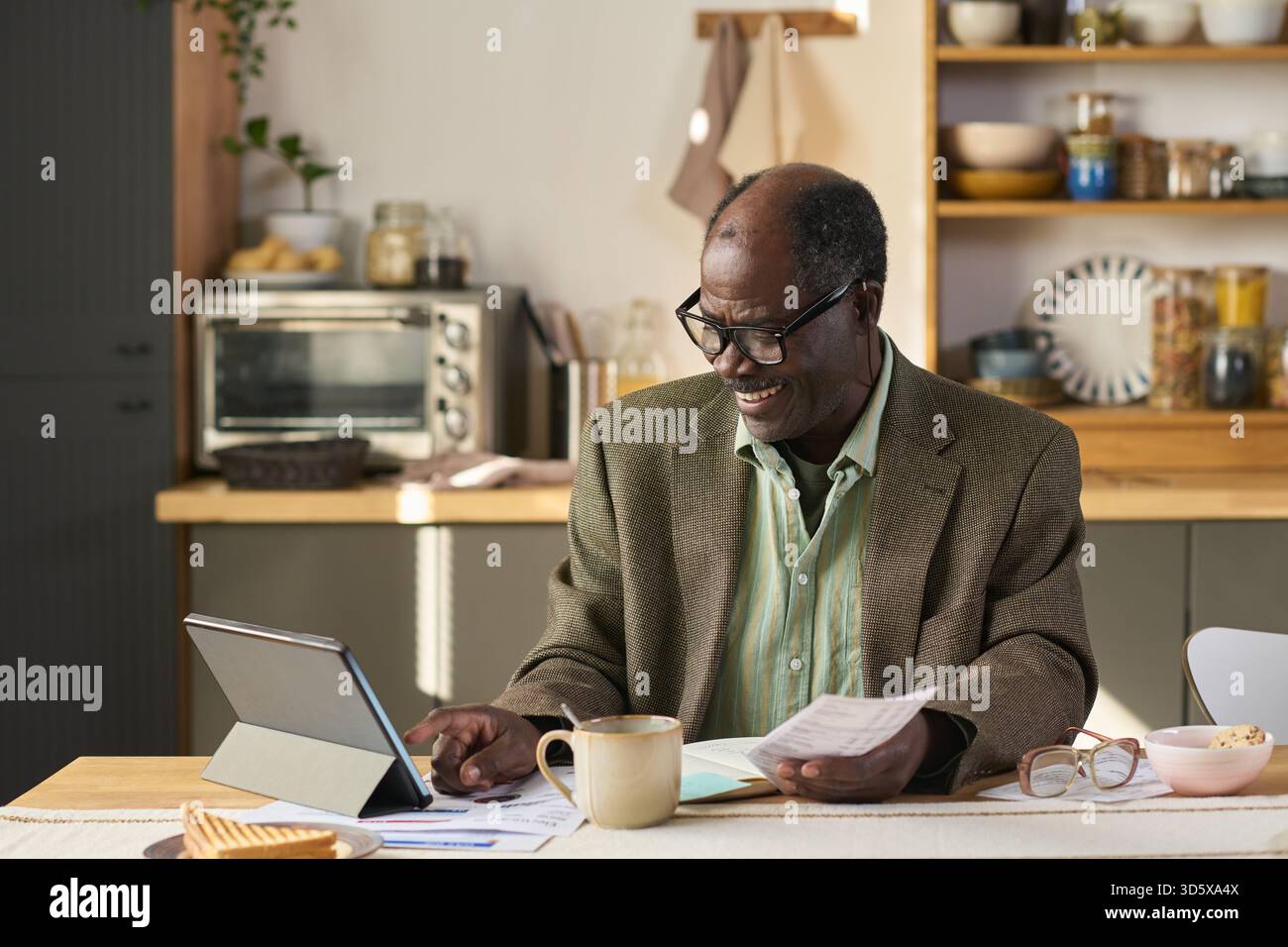 Senior Black Man Using Digital Tablet While Reviewing Financial Documents Stock Photo