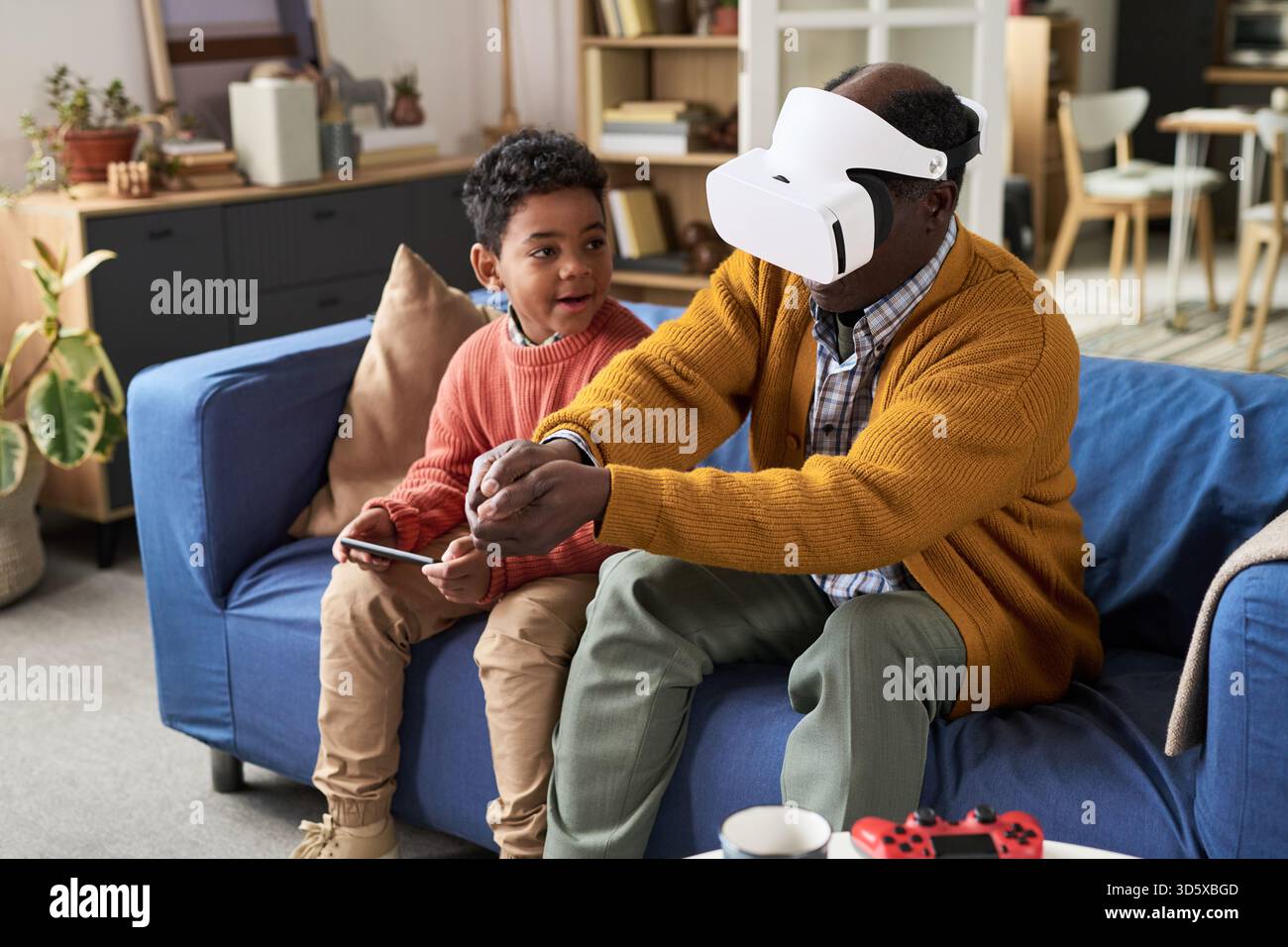 Mature Black Man Using Virtual Reality Headset Sitting with Boy Stock Photo
