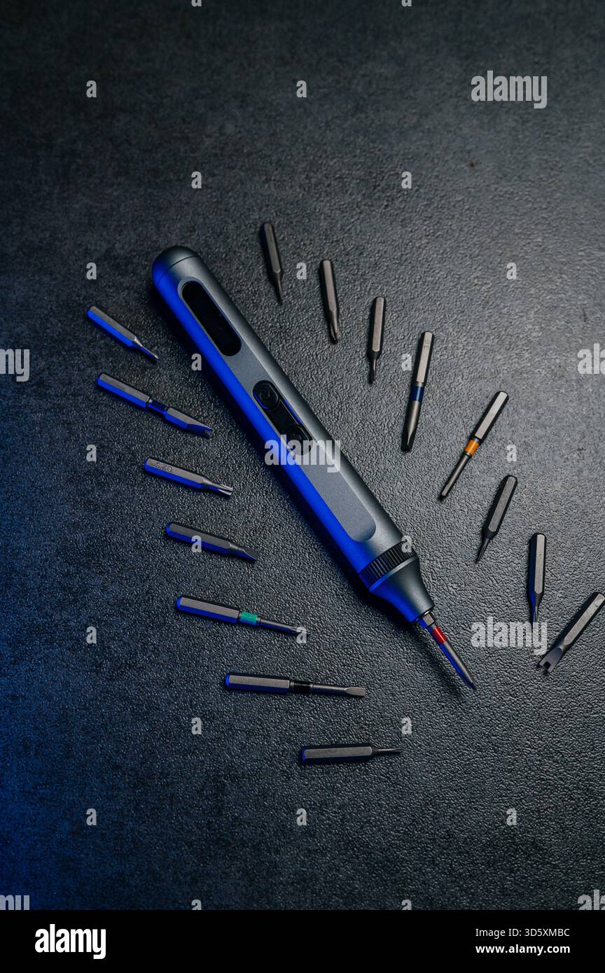 precision electric screwdriver and bits displayed on textured dark surface, product showcase for tool designer, cool blue rim lighting, scattered prec Stock Photo