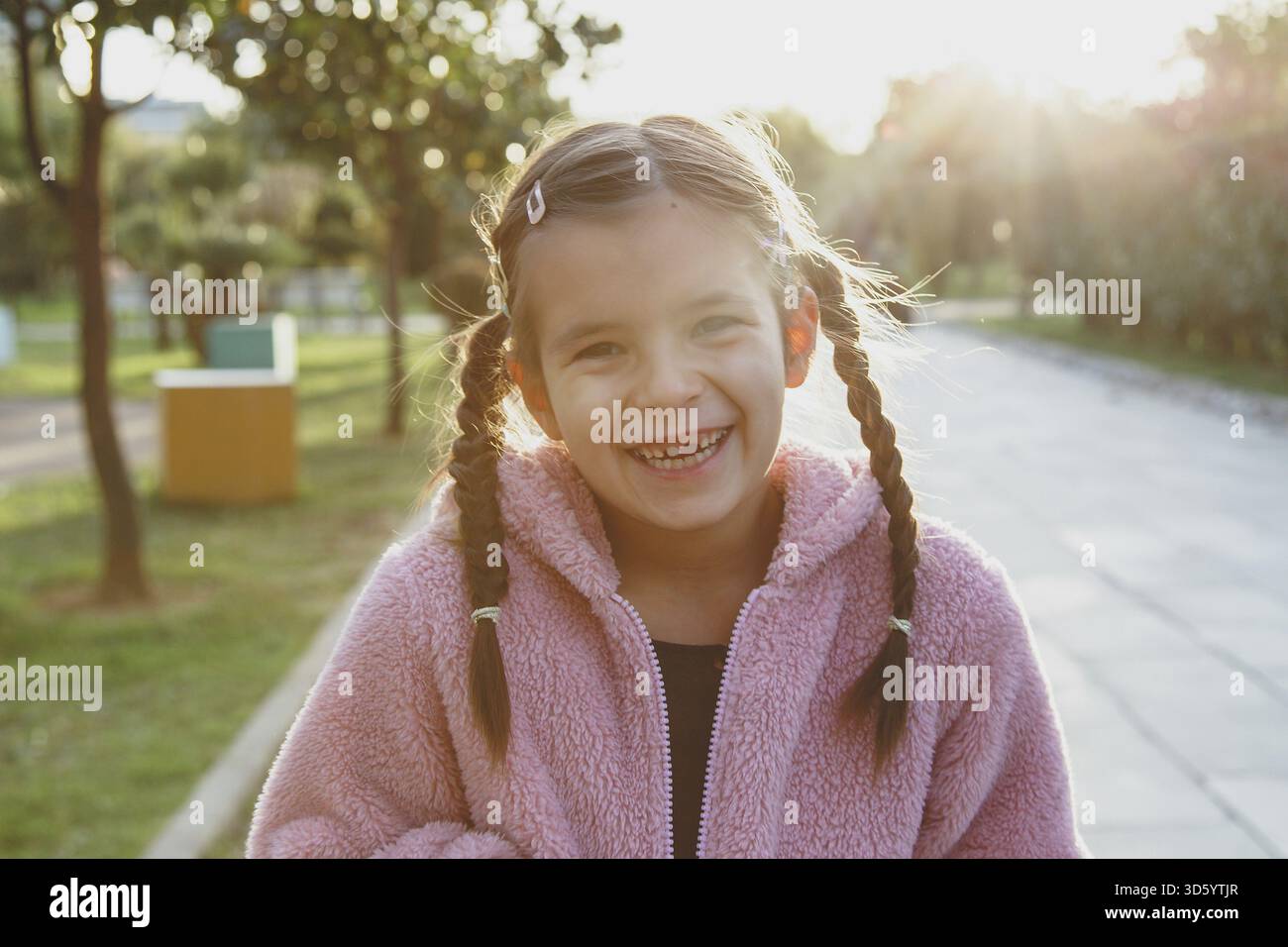 Portrait of a laughing funny cheerful girl 6 years old in the park at sunset, missing front tooth Stock Photo
