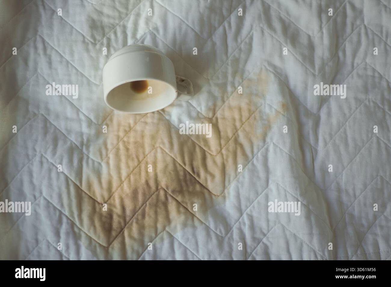 Coffee spill on a white quilted blanket creating a stain Stock Photo