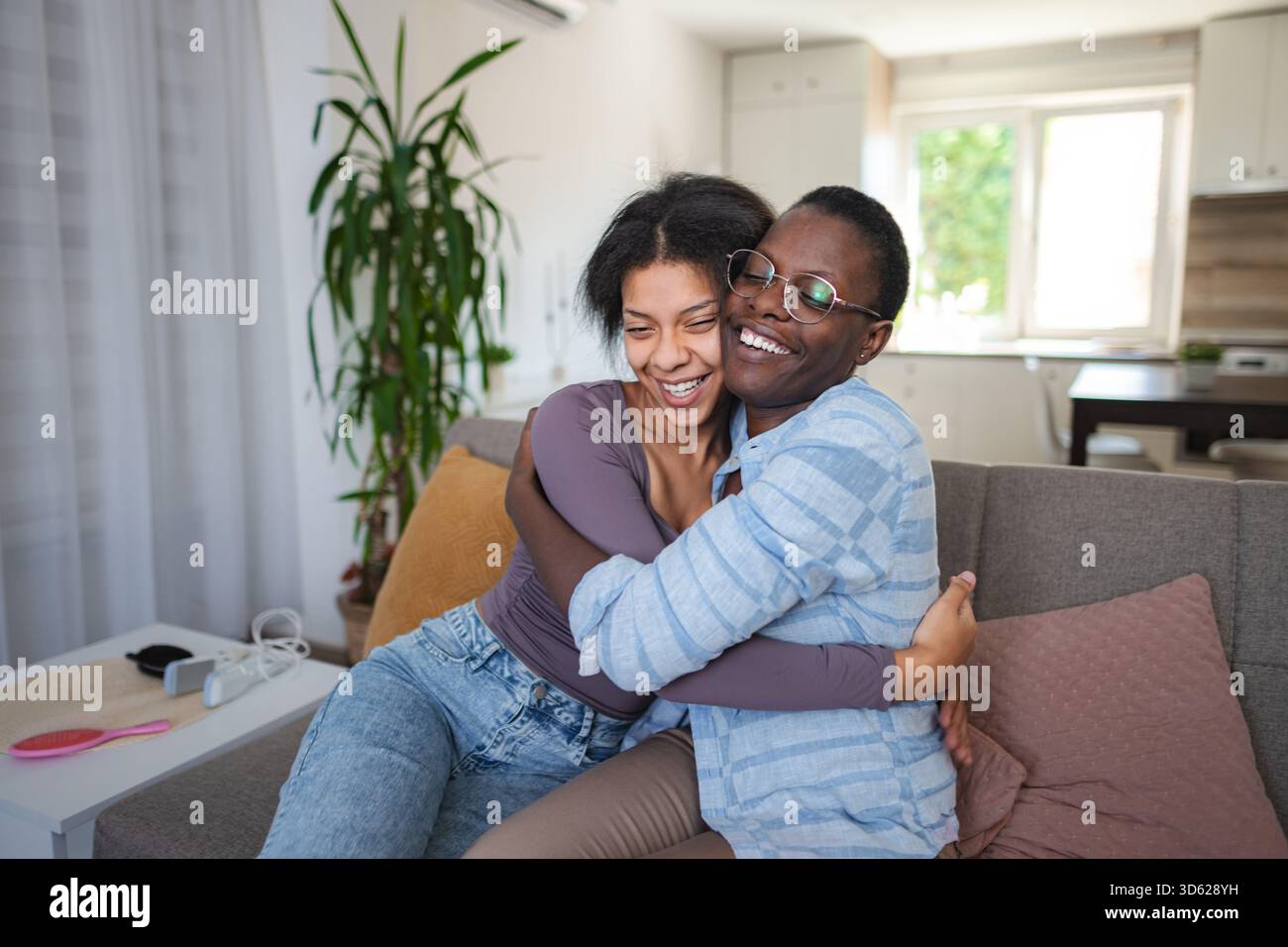 Two joyful friends hugging and laughing on the sofa at home Stock