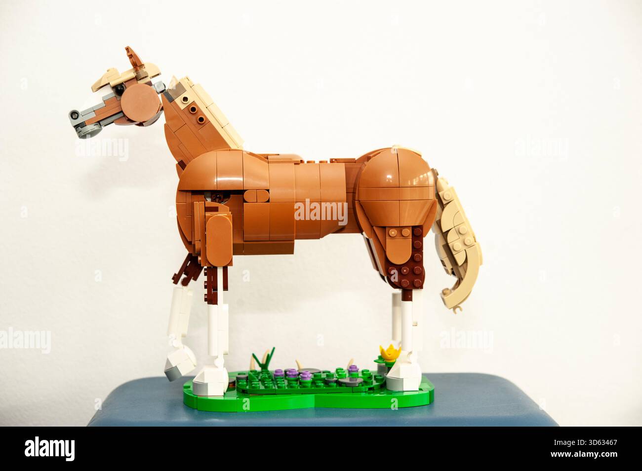 A detailed LEGO horse sculpture built from brown and tan plastic bricks, standing on a small green base Stock Photo