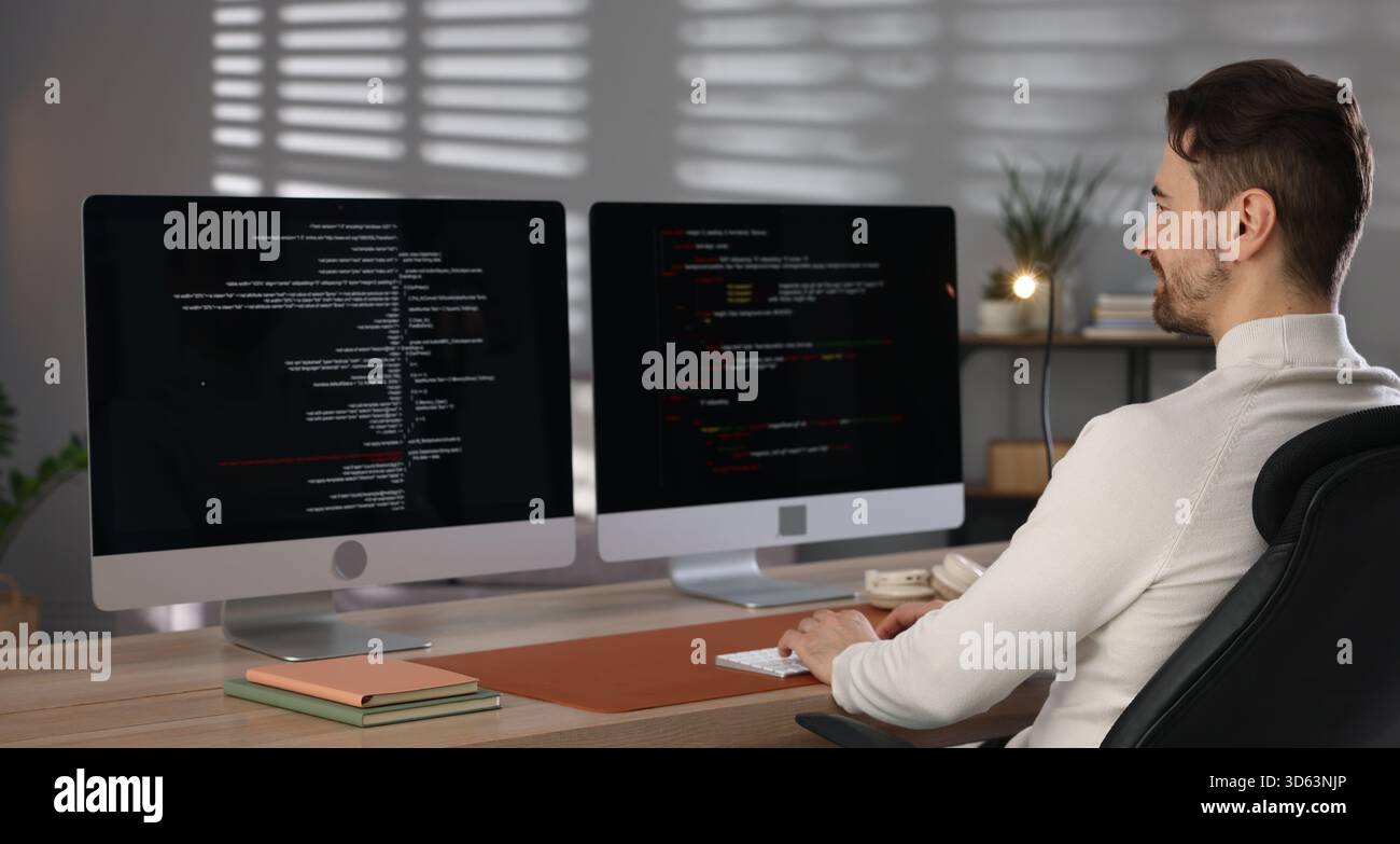 Programmer working on computer with dual monitors at table in office Stock Photo