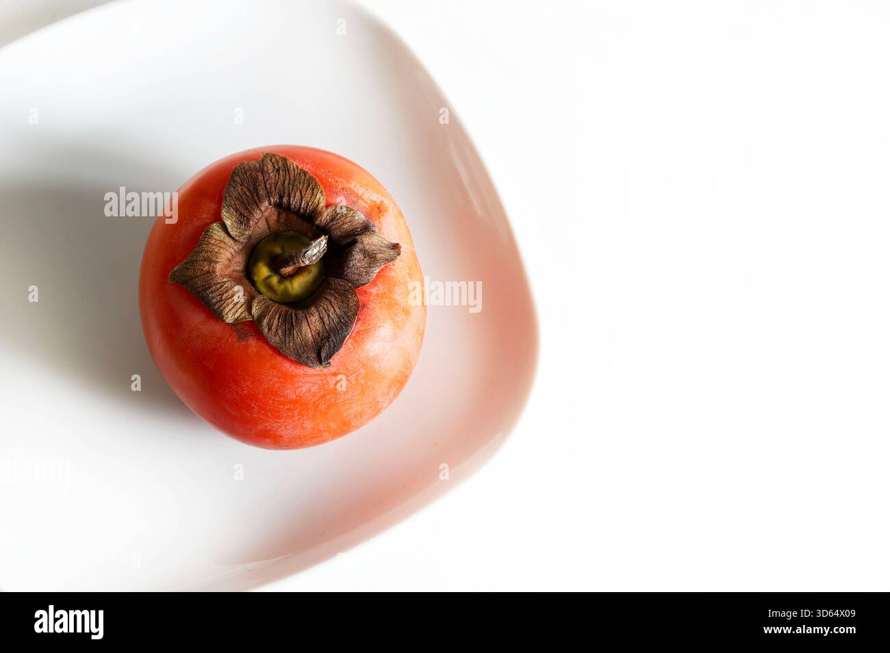 One ripe persimmon in a plate isolated on a white background. Diospyros kaki. Healthy autumn fruit. Overhead view. Stock Photo