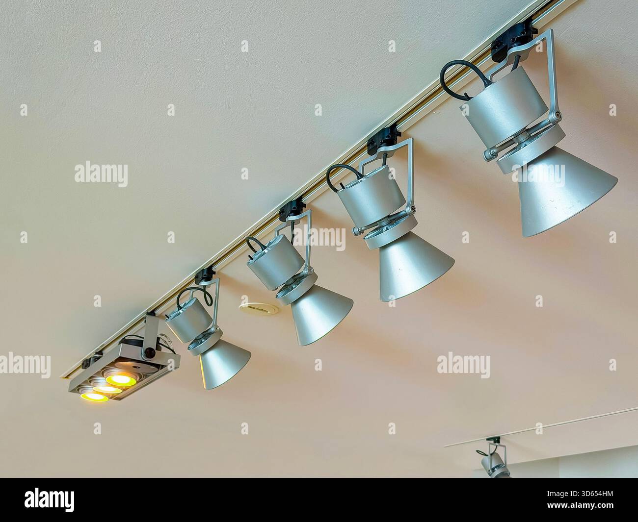 Modern ceiling-mounted track lighting system with multiple adjustable metal spotlights positioned in a row indoors - Smartphone Captured Stock Image