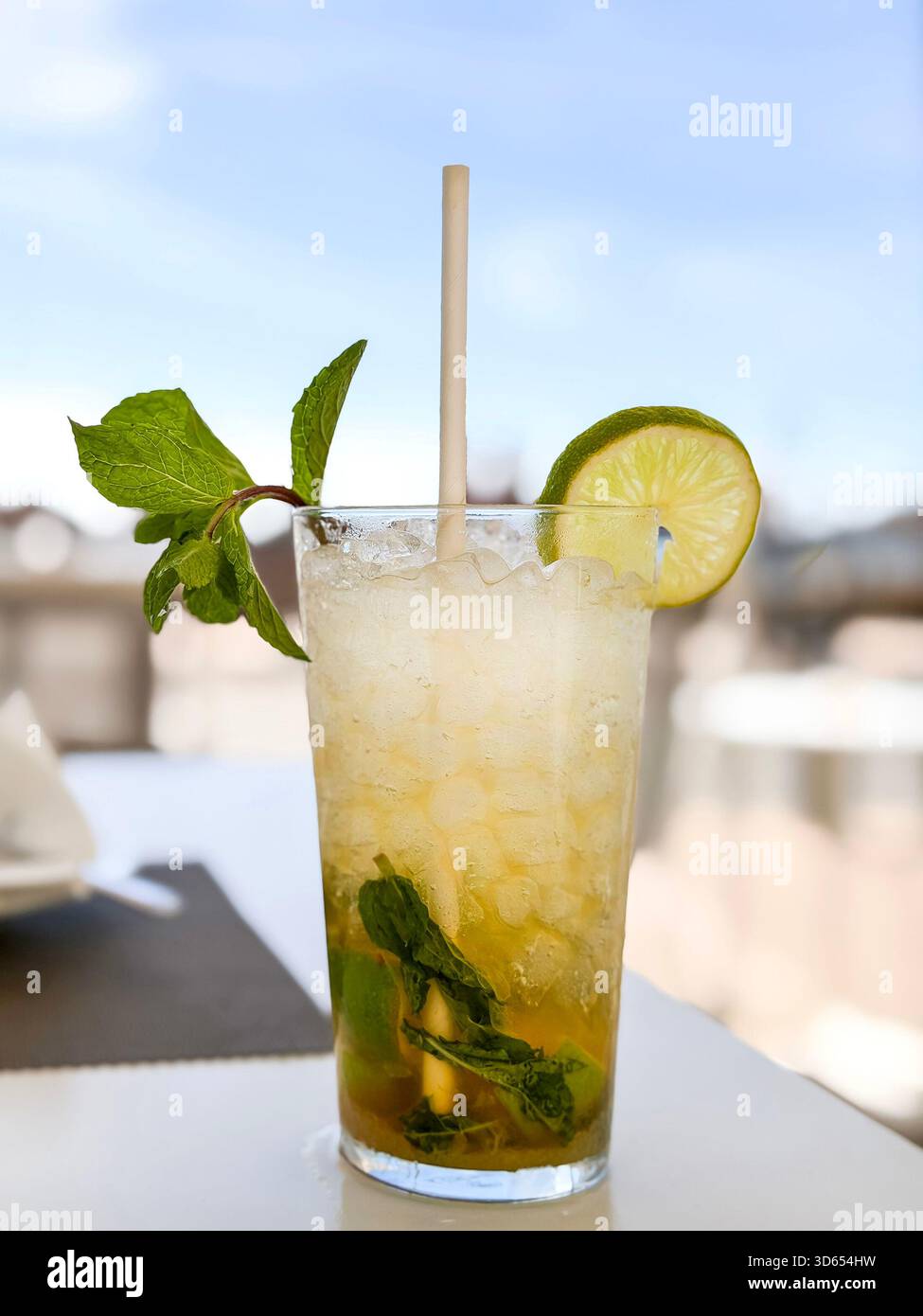 Iced mojito cocktail served in a tall glass with mint leaves, crushed ice, lime slice and paper straw on an outdoor cafe table mallorca spain - Smartphone Captured Stock Image