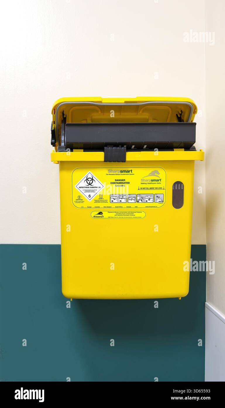 Yellow clinical waste bin mounted on wall inside hospital examination room for safe disposal of biohazardous and sharps waste - Smartphone Captured Stock Image