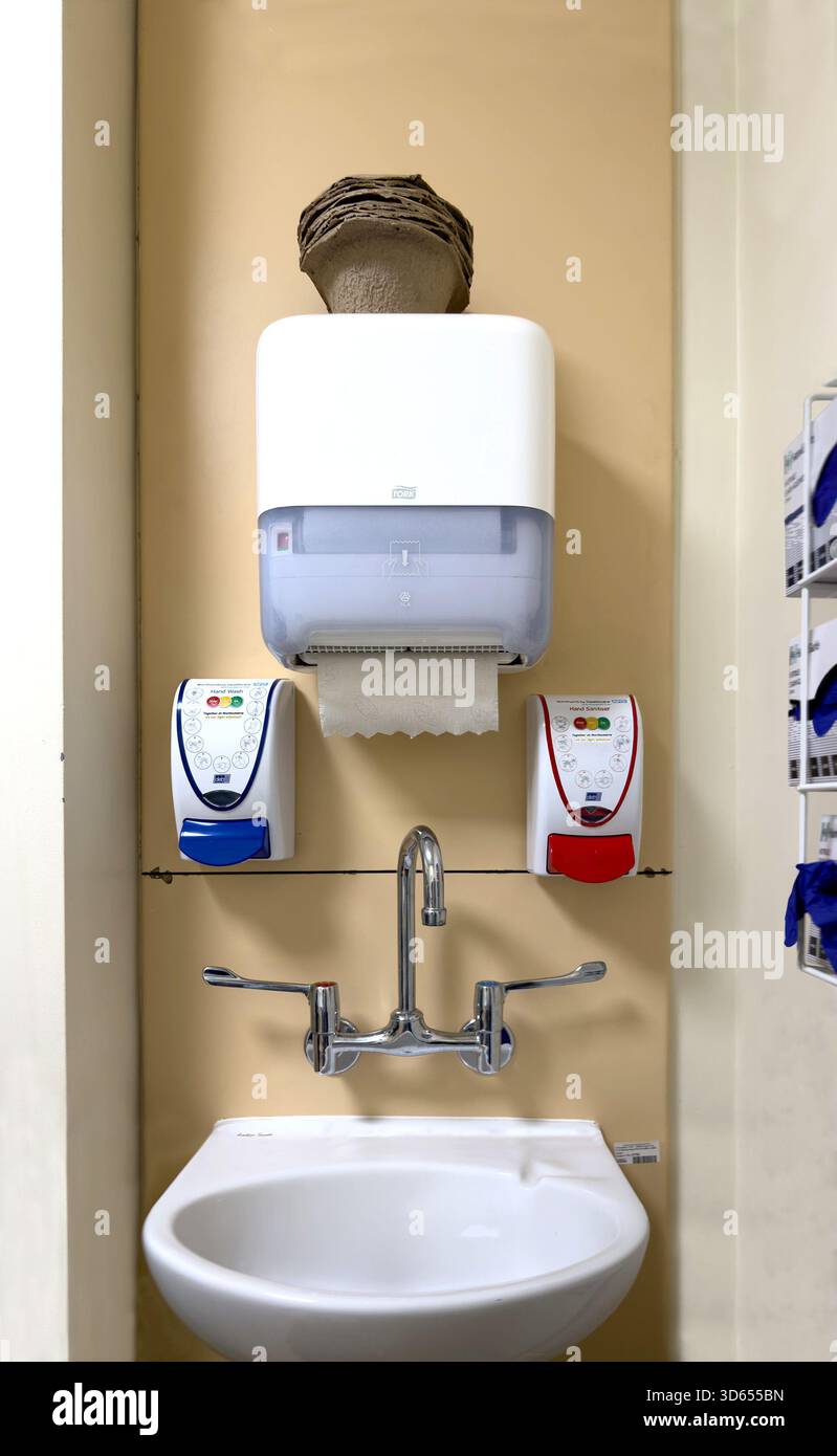 Wall-mounted sink with dual soap dispensers and a paper towel dispenser in a clean medical hospital hygiene station - Smartphone Captured Stock Image