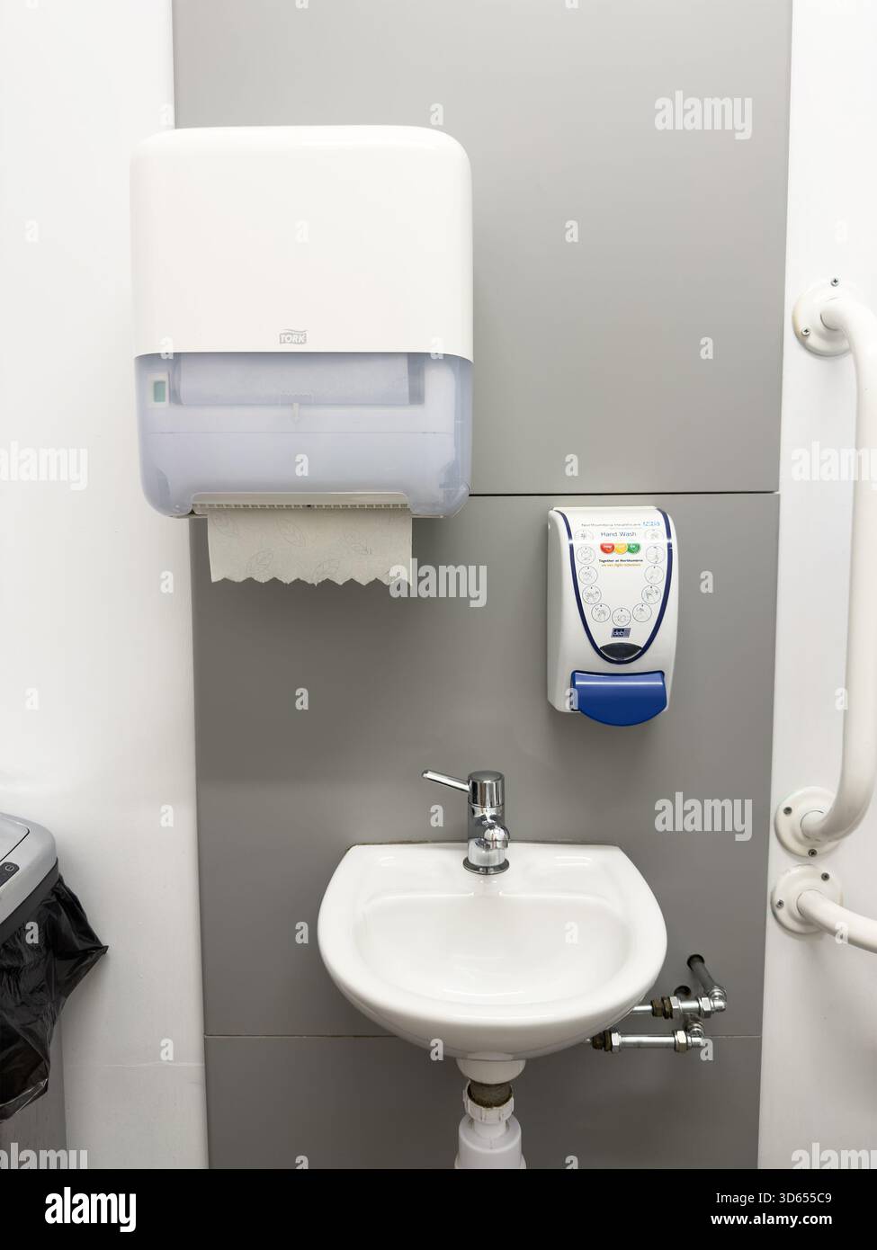 Wall mounted paper towel dispenser and soap dispenser above a small white sink in a clean public washroom with accessibility features - Smartphone Captured Stock Image