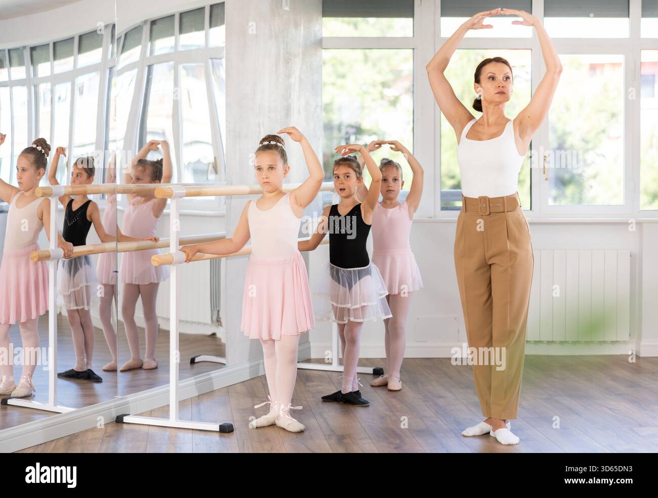 Girl students of choreographic school look at woman teacher and repeat ...