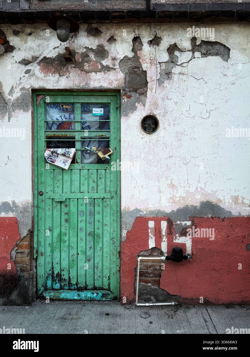 Weathered green wooden door with peeling paint and old mail on a deteriorating stucco wall in an urban street setting - Smartphone Captured Stock Image
