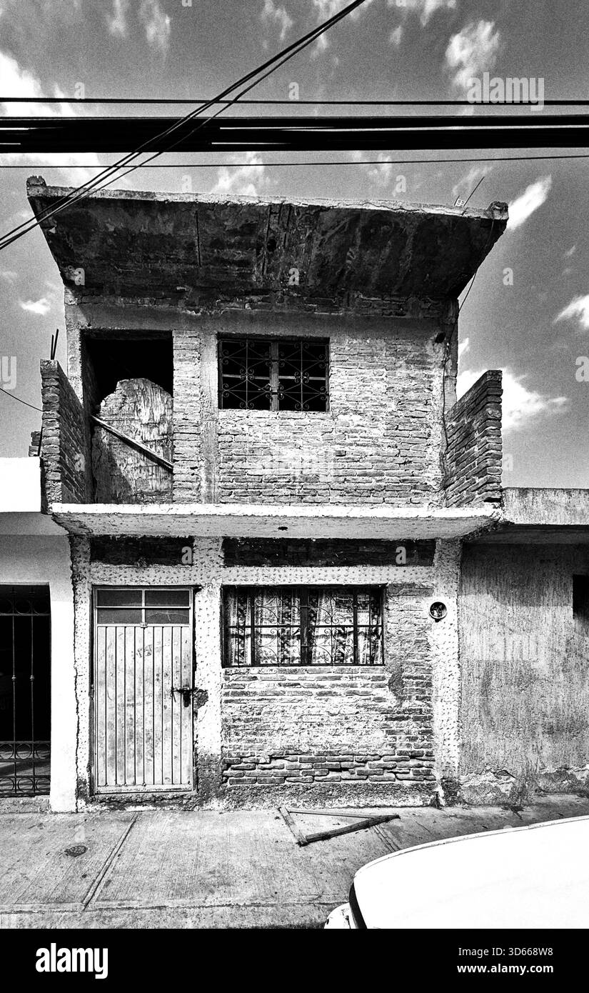 Black and white image of a modest unfinished brick house with exposed concrete and metal door in a residential urban area - Smartphone Captured Stock Image